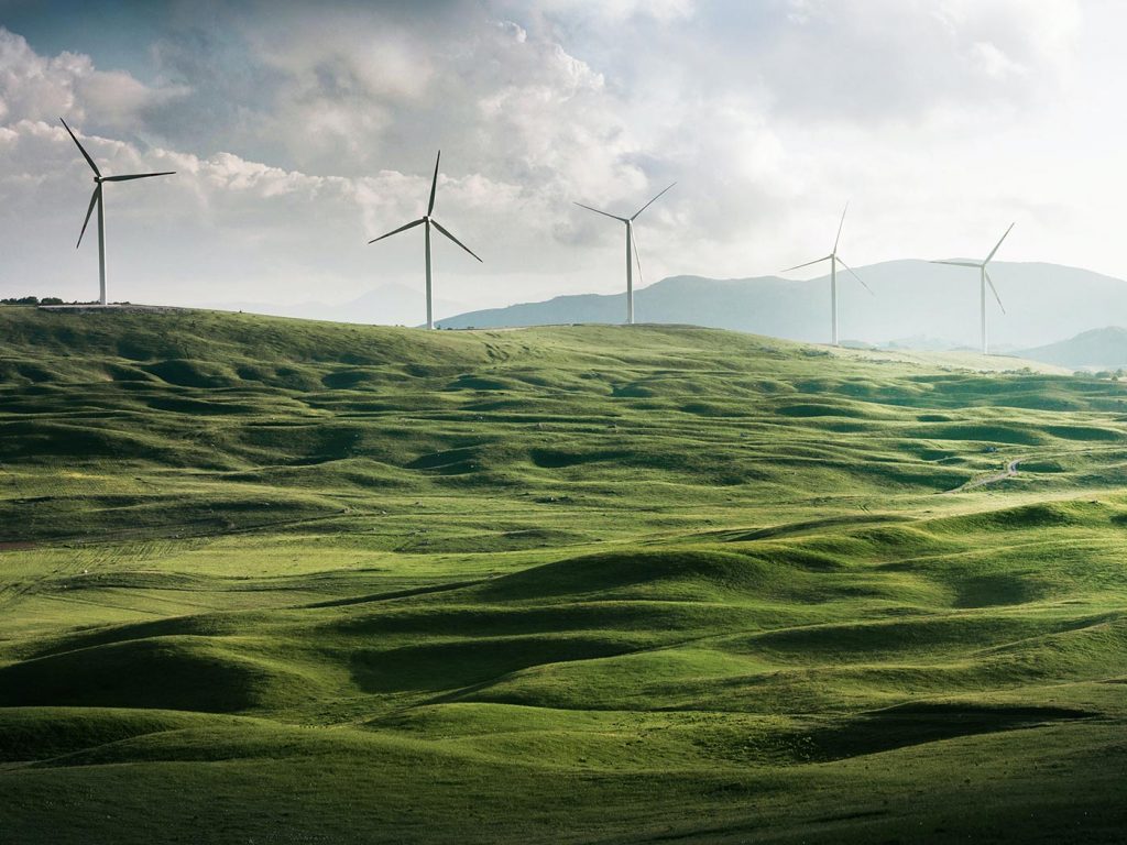 Windmills in a rolling green field overlooked by a mountain